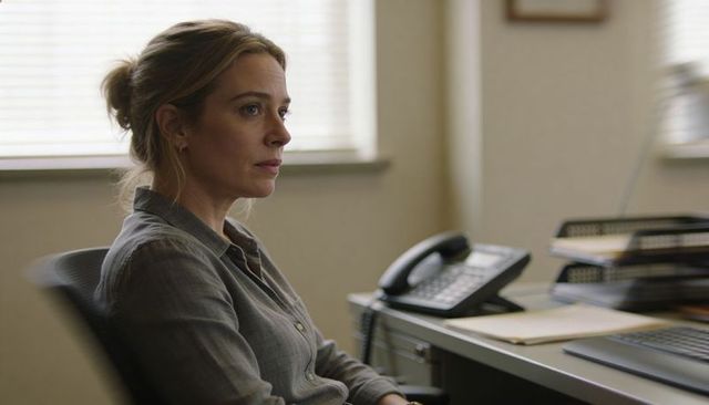 Woman in modern office looking thoughtful while organizing files at desk with telephone