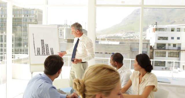 Senior Businessman Presenting Graph to Colleagues During Meeting in Modern Office - Download Free Stock Images Pikwizard.com