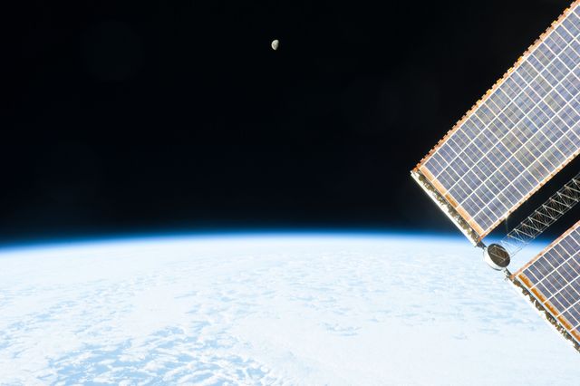 Visual depicting moonrise from perspective of International Space Station, showing Earth's curvature, solar panels of ISS in foreground and vastness of outer space. Ideal for educational resources, space exploration articles and science presentations.
