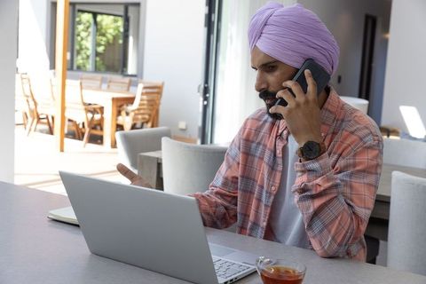 Professional man in turban using smartphone at modern workspace