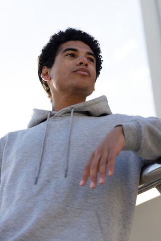 Upward-gazing african american teen in gray hoodie leaning on rail urban backlit portrait