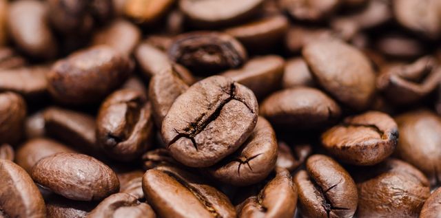 This high-quality macro shot shows roasted coffee beans in great detail, emphasizing their rich texture and deep brown color. Ideal for use in marketing materials for coffee shops, ads for coffee products, culinary blogs, and websites focused on food and beverages. The image conveys themes of freshness, aroma, and quality associated with coffee.