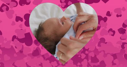 Mother fastening onesie on newborn boy through heart frame with pink heart background