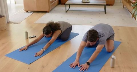 African american couple practicing yoga and stretching on blue mats in bright living room