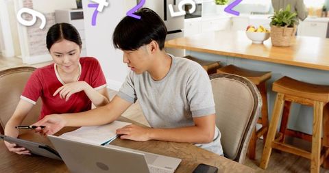 Young couple studying together at kitchen table with laptop, tablet and notes