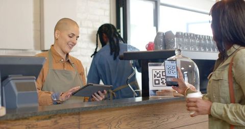 Barista smiling while taking order and customer scanning qr code for contactless payment