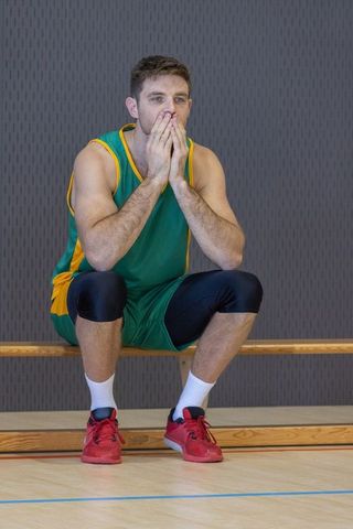 Basketball player contemplating on courtside bench