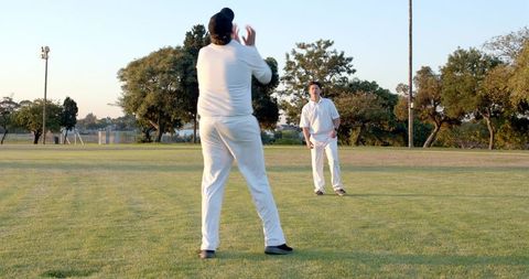 Two cricketers practicing catching on green field at golden hour