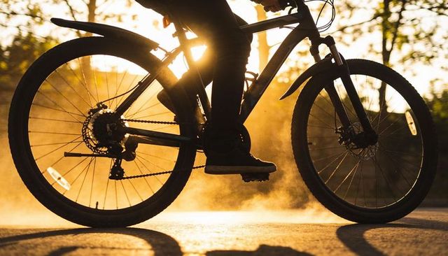 Silhouetted cyclist pedaling through golden dust on sunlit pavement at golden hour