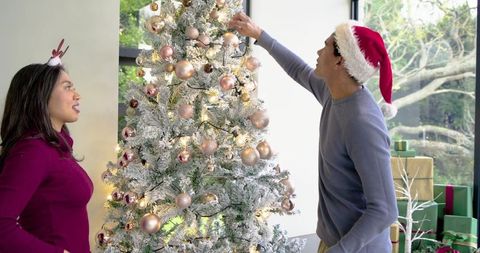 Couple decorating flocked christmas tree with rose gold ornaments and presents