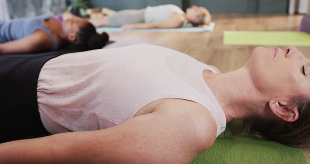 Women laying peacefully on exercise mats during a yoga class, practicing Savasana pose. Perfect for promoting wellness, mindfulness, relaxation techniques, fitness classes, and workout routines in a serene environment.