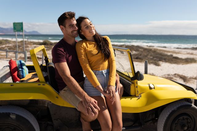 Happy caucasian couple sitting on beach buggy by the sea embracing and smiling in the sun. beach stop off on romantic summer holiday road trip.