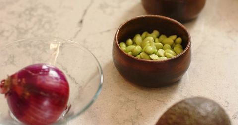 Rustic kitchen prep with shelled edamame in wooden bowl and red onion on marble countertop