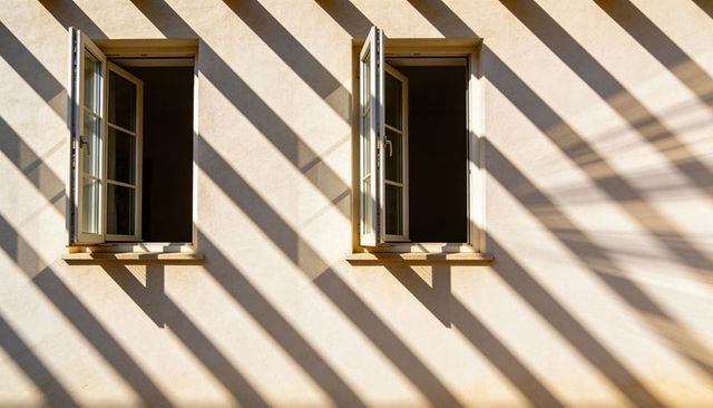 Sunlit Beige Facade with Twin Open Casement Windows and Dramatic Diagonal Shadow Bands