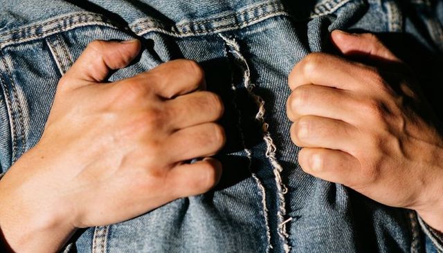 Hands gripping frayed denim jacket tight close-up showing texture, grip, and rugged detail