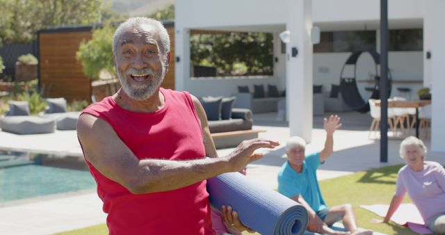 This image depicts a smiling senior man holding a yoga mat in an outdoor setting, with other seniors in background. Ideal for promoting active lifestyle, senior community activities, wellness programs, and exercise routines for elderly individuals.