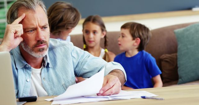 Stressed Father Reviewing Financial Documents at Home with Children in Background - Download Free Stock Images Pikwizard.com