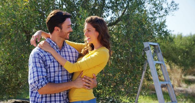 Smiling couple embracing in garden on sunny day. Perfect for relationship, love, and romance themes. Useful for advertisements, social media posts, and blogs discussing happy relationships and outdoor activities.