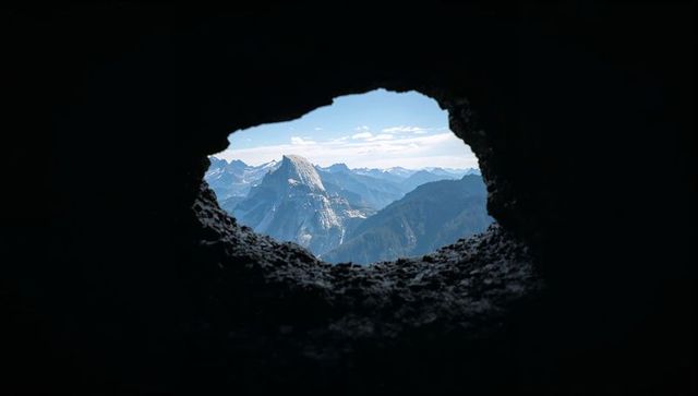 Cave opening framing granite peak and layered mountain ridges in soft morning light