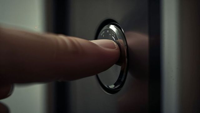 Fingertip pressing chrome push button on modern metallic control panel close-up high-tech
