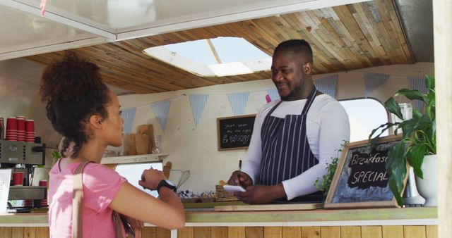 Smiling african american male food truck owner taking order from happy female customer. small independent business, street food, service and catering.