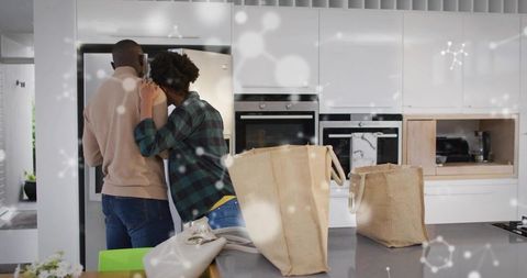 Couple embracing while unloading grocery totes in modern minimalist kitchen placing reusable bags