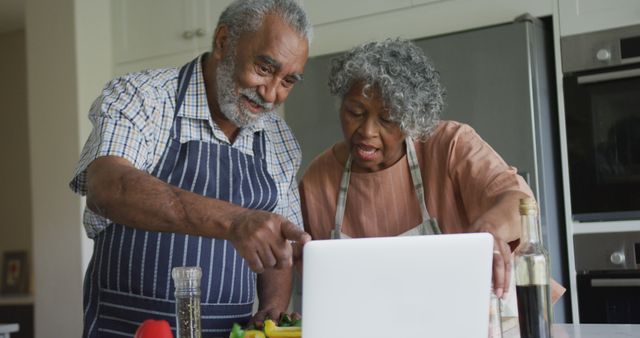 Happy african american senior couple cooking together, using laptop. healthy, active retirement lifestyle at home.