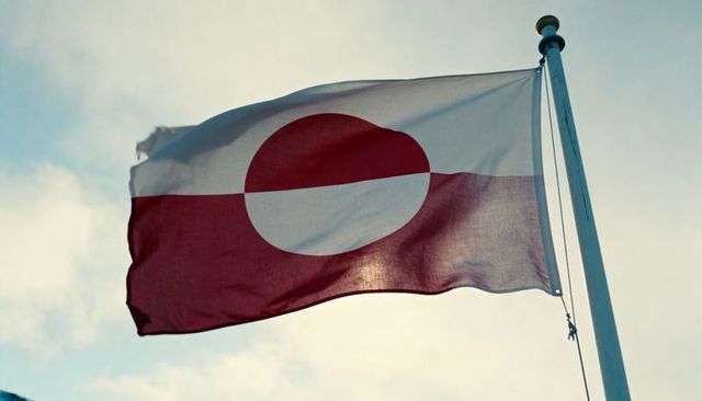 Waving greenland flag featuring split red-white disk design backlit against cloudy sky