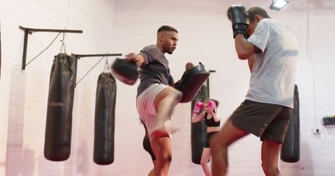 Boxing coach holding pads while trainee executing kick in urban gym training