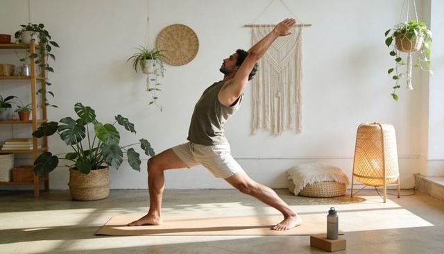 Man practicing warrior lunge yoga pose in sunlit bohemian minimalist living room