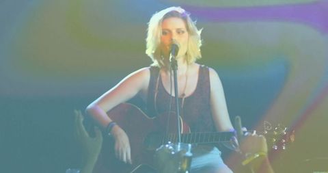 Teenage Musician Strumming Guitar Under Vibrant Lights on Stage