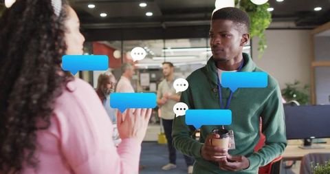 Professional holding coffee chatting with colleague in open office with digital chat bubbles