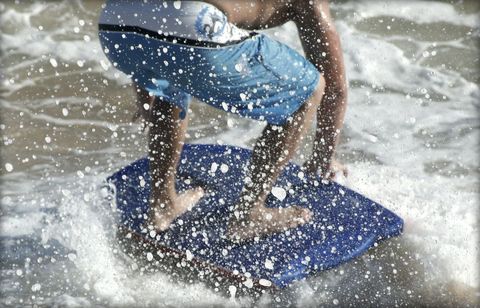 Person Skimboarding in Ocean Waves with Water Splash