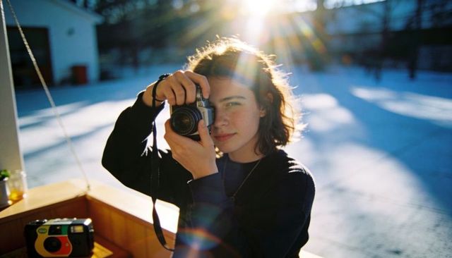 Young photographer holding film slr camera with sunlit lens flare in outdoor courtyard