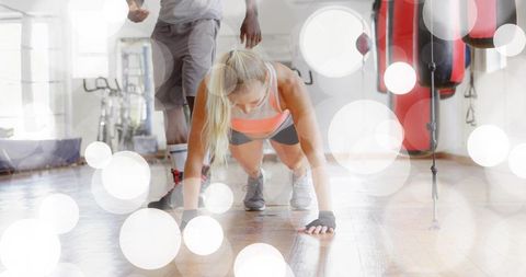 Female athlete performing plank with trainer in bright boxing studio on hardwood floor