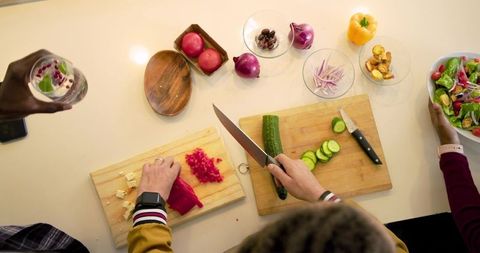 Diverse friends chopping cucumber and cheese preparing fresh salad at kitchen counter