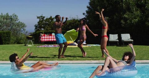Friends enjoying backyard pool party, dancing and floating on vivid inflatable rings