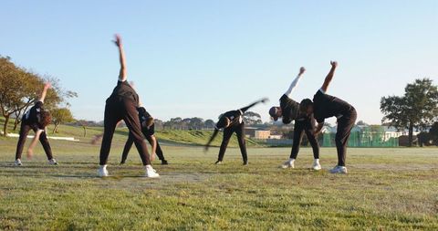 Group of Athletes Performing Morning Stretching Routine on Grass Field