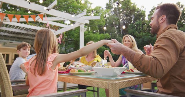 Happy caucasian parents, children and grandparents holding hands say grace at dining table in garden. Religion, tradition, summer, family, meal, celebration, togetherness and lifestyle, unaltered.