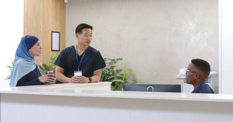 Multicultural healthcare team chatting at clinic reception desk in navy scrubs promoting teamwork