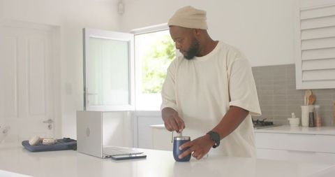 African american man preparing coffee while working remotely at minimalist kitchen island