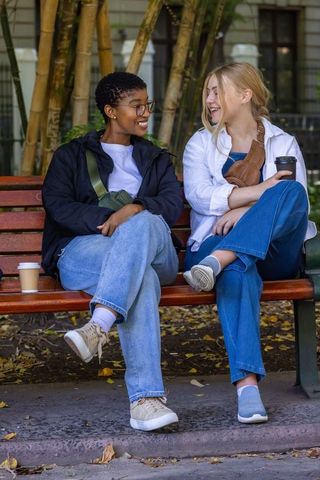 Diverse friends chatting on park bench holding coffee, smiling in casual denim outdoor courtyard