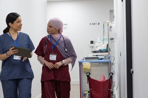 Multicultural female nurses walking and consulting in radiology corridor with tablet