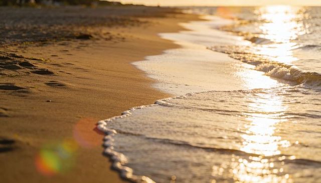 Glistening golden-hour shoreline with gentle waves, wet sand, seafoam and footprints