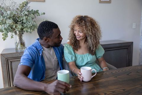 Sharing morning coffee multiracial couple smiling over pastel mugs at rustic dining table
