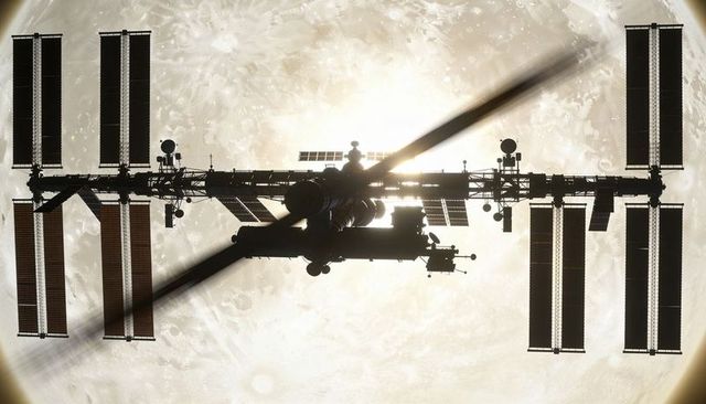 Silhouetted Modular Space Station Crossing Moon Backlit by Lunar Glow, Solar Arrays and Robotic Arm