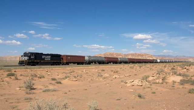 Diesel locomotive pulling freight of tanker cars across arid desert with red mesas