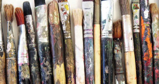Used paintbrushes with varying amounts of paint, showcasing a mix of colors on handles and bristles, arranged horizontally on a white surface. This close-up image emphasizes creativity, artistic process, and the tools essential for painting. Ideal for use in articles, blogs, or websites focusing on art, creativity, and painting tutorials.