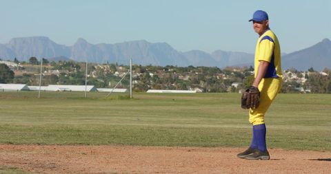 Baseball Player Standing on Infield Wearing Yellow and Blue Uniform Holding Leather Glove