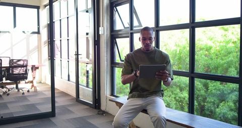 African man using tablet in modern coworking space by large greenery-filled windows